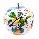 A decorative apple-shaped object with a white base and hand-painted multicolor designs, including green leaves, black branches, a blue top section, yellow background areas, and small red and black details.