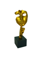 Gold mask sculpture with a hand covering its mouth on a black base against a white background